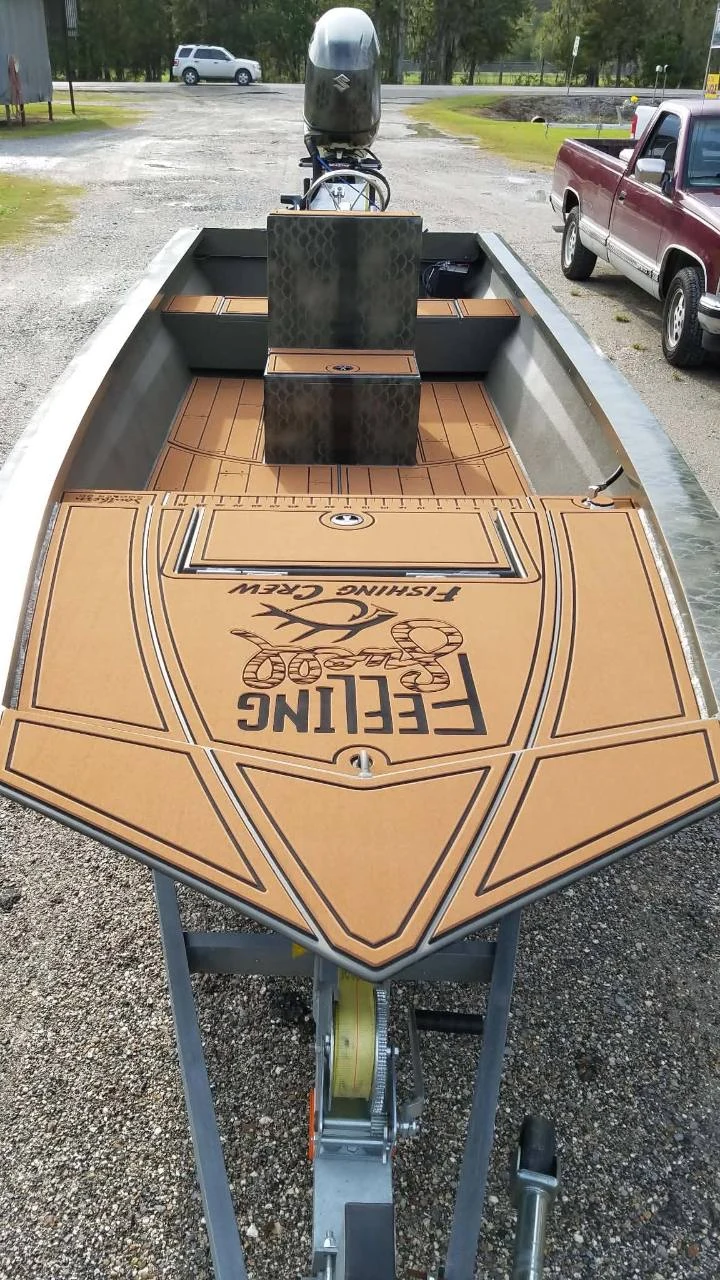 Aluminum boat interior with tan patterned decking, storage hatches, a center console, and an outboard motor