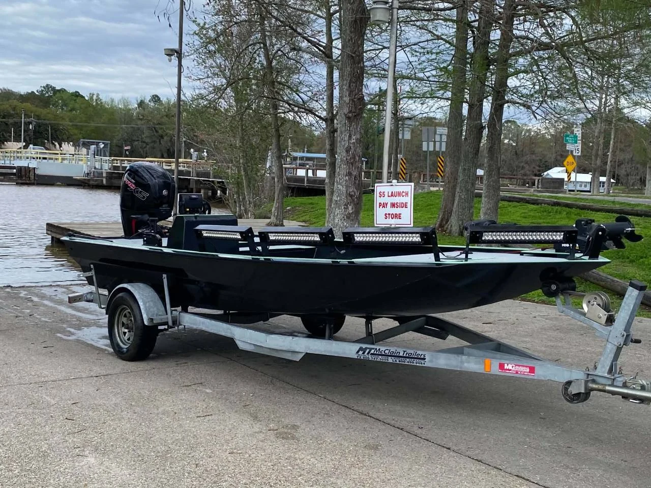 Black aluminum boat with outboard motor and deck lights on a trailer at a boat launch